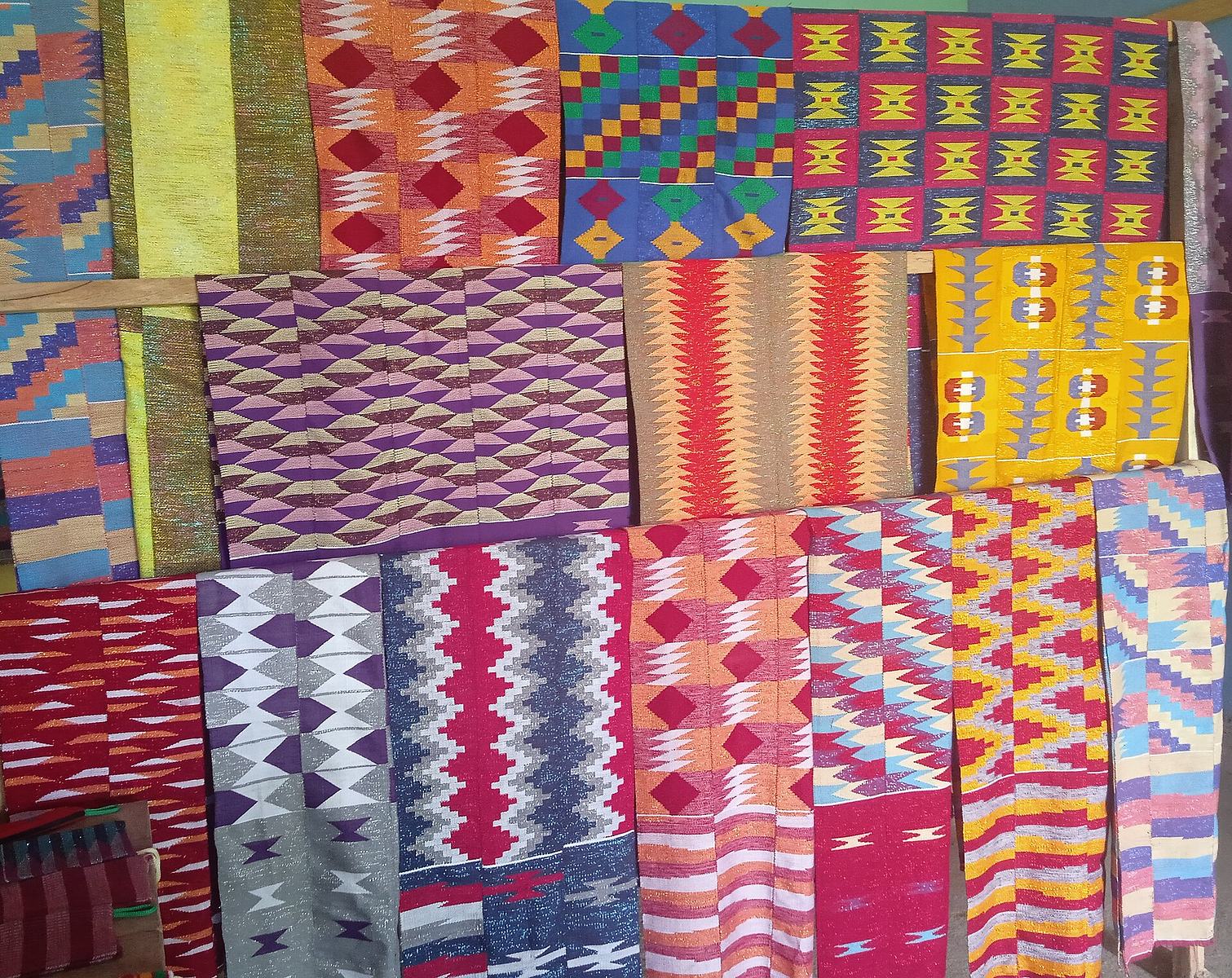 Several folded kente cloths with different colourful designs from the Volta region of Ghana.