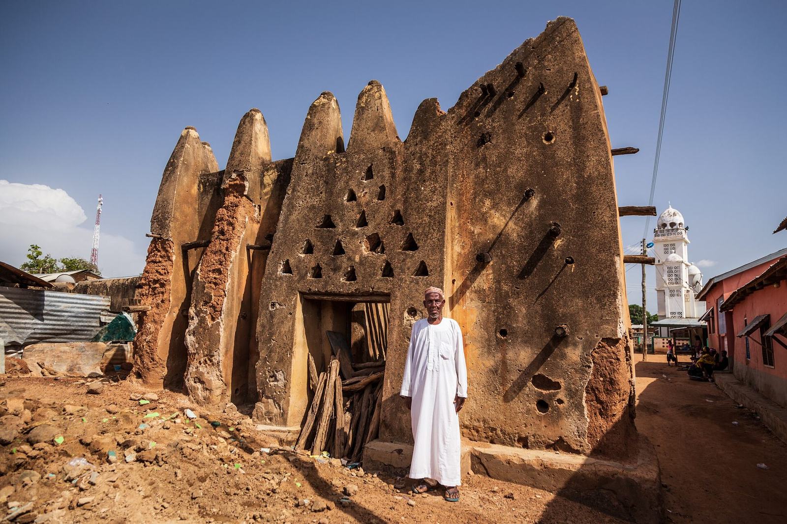 Earthen mosque at Dondoli with a man standing in front of its wall.